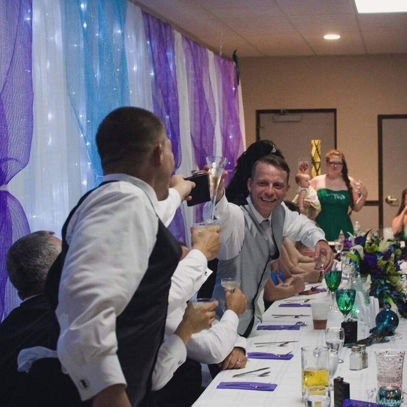 Jay raises a glass with a groomsman during the toasts at the head table at the Owego VFW, with Cassandra just behind him