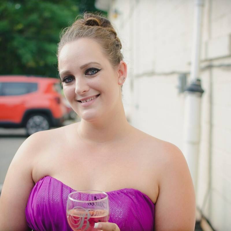 A bridesmaid in a magenta strapless dress smiling with a glass of wine outside on the wedding day