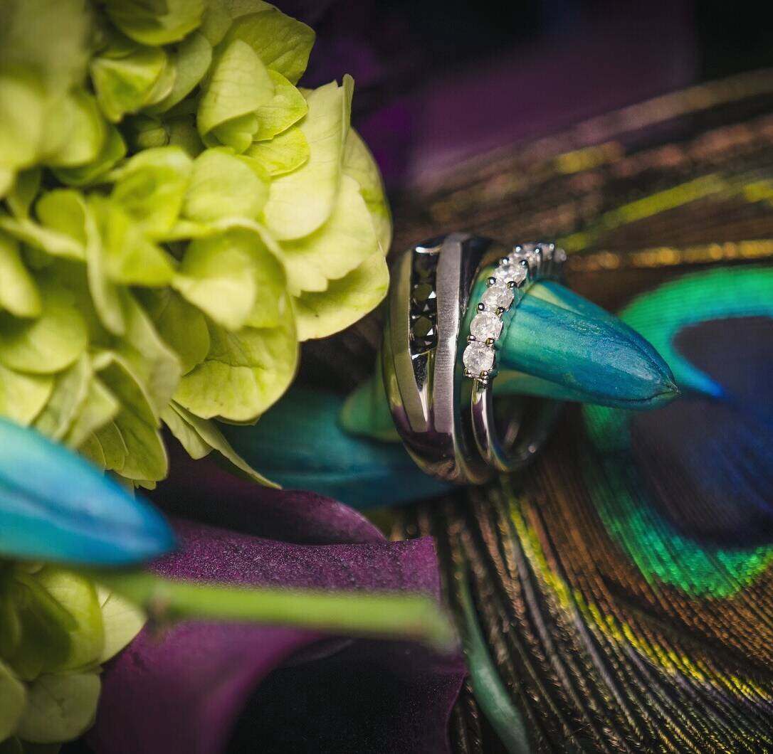 Cassandra and Jay's wedding rings resting on a peacock feather in a lime green and teal bouquet