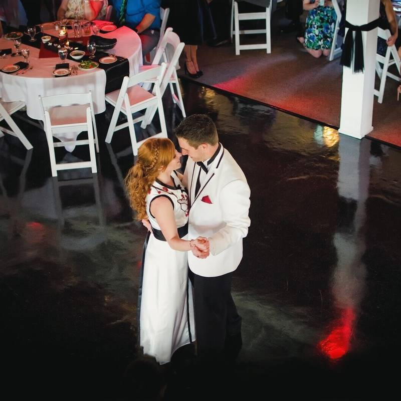 Symphony and Jonathan dance at the Lakewatch Inn reception on a dark polished floor between round tables with red and black settings, seen from above