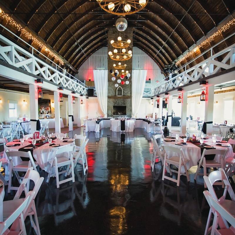 The reception hall at the Lakewatch Inn set for dinner under an arched wooden ceiling and wagon wheel chandeliers, with red and black table settings and white chairs