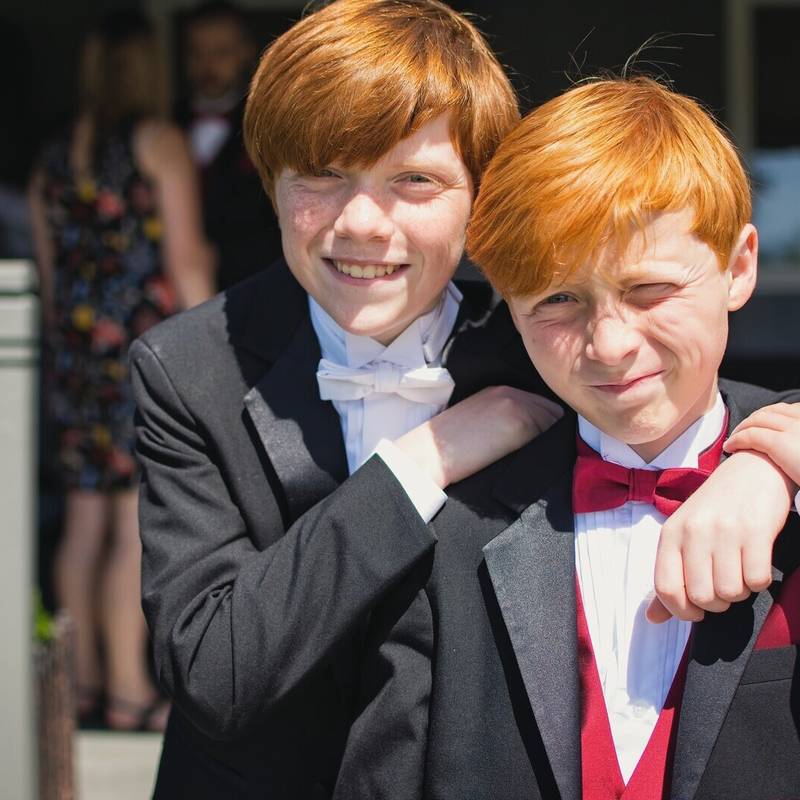The bride's two red haired sons, the ring bearers, in tuxedos with a white bow tie and a red bow tie, arm in arm on a porch