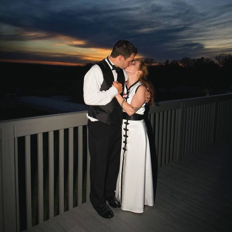 Symphony and Jonathan kiss on a deck at dusk, with the last of the sunset behind them